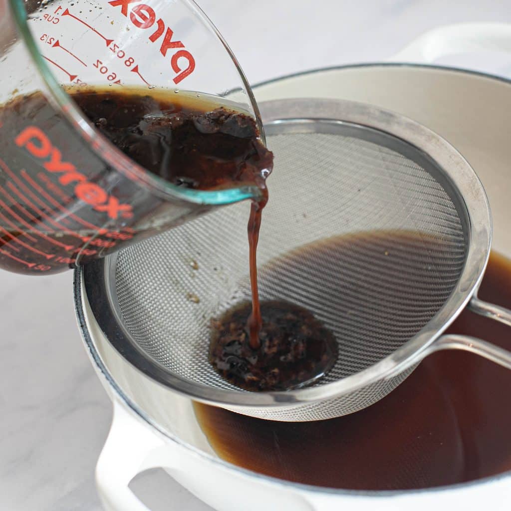 pan drippings being poured through a mesh strainer