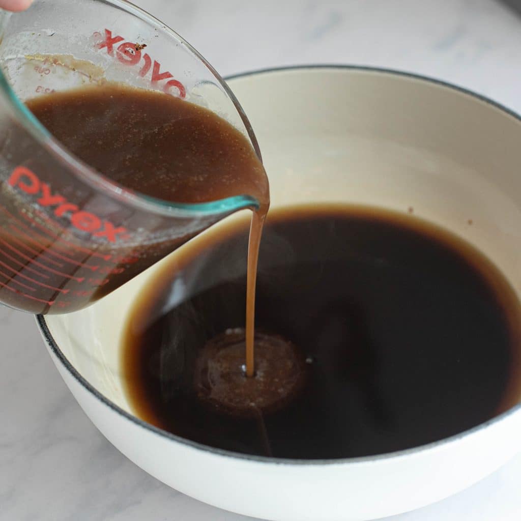 turkey pan drippings pouring into a pot of prepared gravy